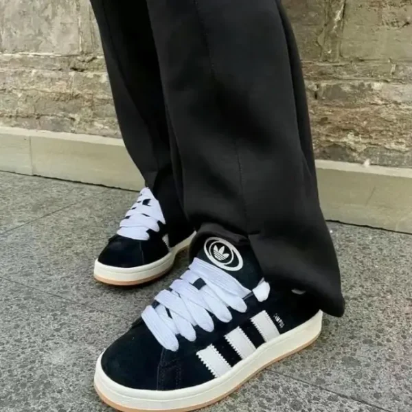 Adidas Campus 00s Black styled on a man wearing black trousers, showcasing the sneaker’s premium black suede, chunky rubber sole, and classic 3-Stripes branding