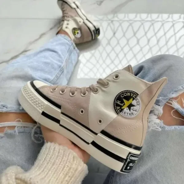 Converse Chuck 70 High Plus ‘Logo Collage – Beach Stone’ worn by a woman in blue jeans, showcasing asymmetrical canvas paneling, stitched vintage logo collage, and high rubber foxing