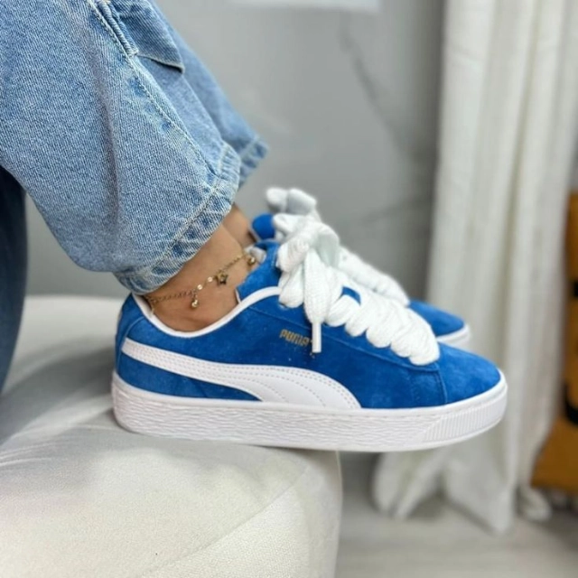 Puma Suede XL Royal Blue styled on a lady wearing blue jeans and a leg bracelet, showcasing the sneaker’s premium royal blue suede and chunky rubber sole